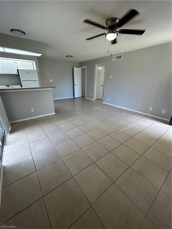 1989 Rookery Bay Drive, Unit 704 Naples, FL 34114 - Photo 3 of 10 Unfurnished living room featuring light tile patterned floors, a ceiling fan, and a textured ceiling
