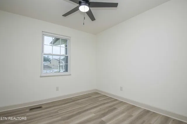 an empty room with wooden floor fan and windows
