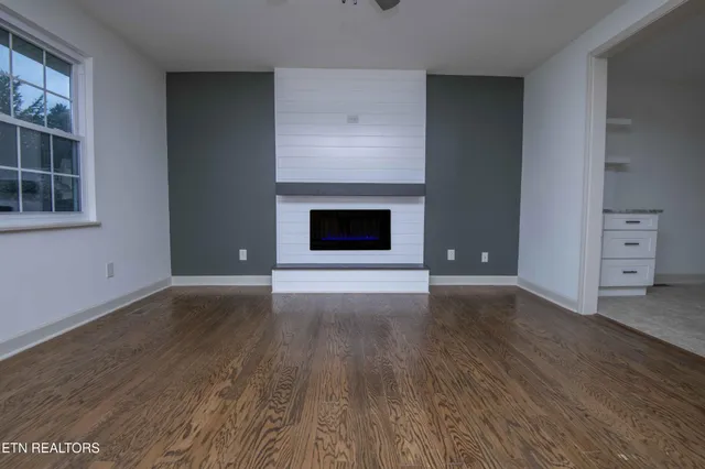an empty room with wooden floor fireplace and windows