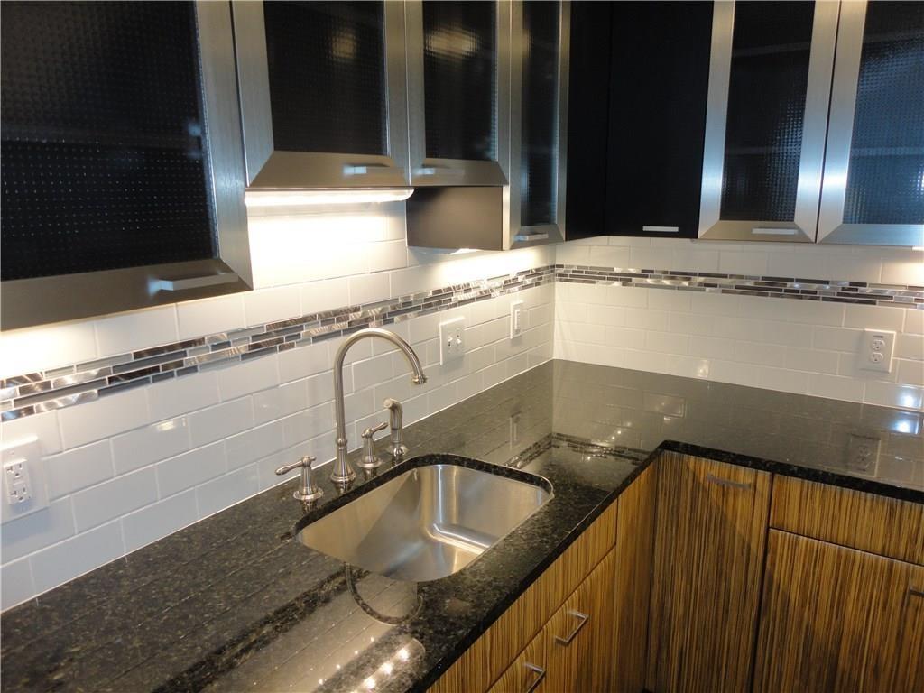 3311 Speedway, Unit D Austin, TX 78705 - Photo 8 of 23 The kitchen features dark granite countertops, a stainless steel sink with a brushed nickel faucet, and a white subway tile backsplash with a decorative mosaic accent
