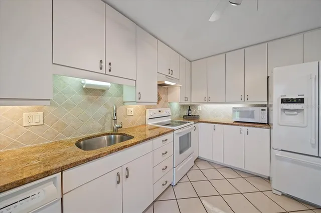 a kitchen with granite countertop white cabinets white appliances and sink