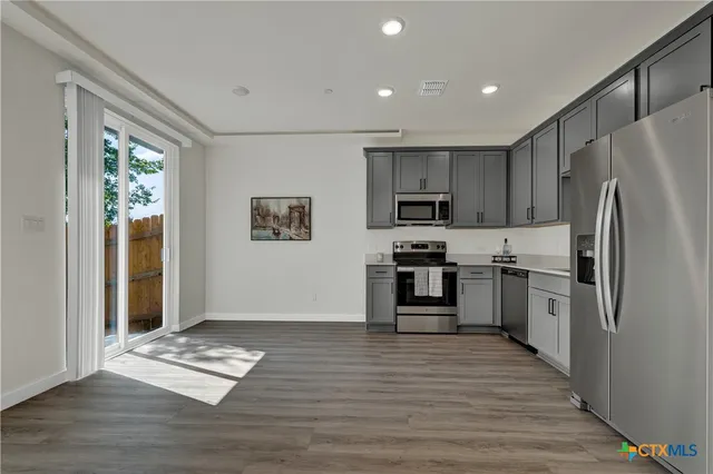 a kitchen with stainless steel appliances granite countertop a refrigerator a stove a microwave a dining table and chairs with wooden floor