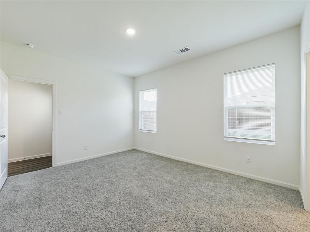 4510 Winecup Road Melissa, TX 75454 - Photo 13 of 22 Spacious room featuring plush gray carpeting, white walls, two windows with blinds, a recessed ceiling light, and an open doorway revealing wood-finish flooring