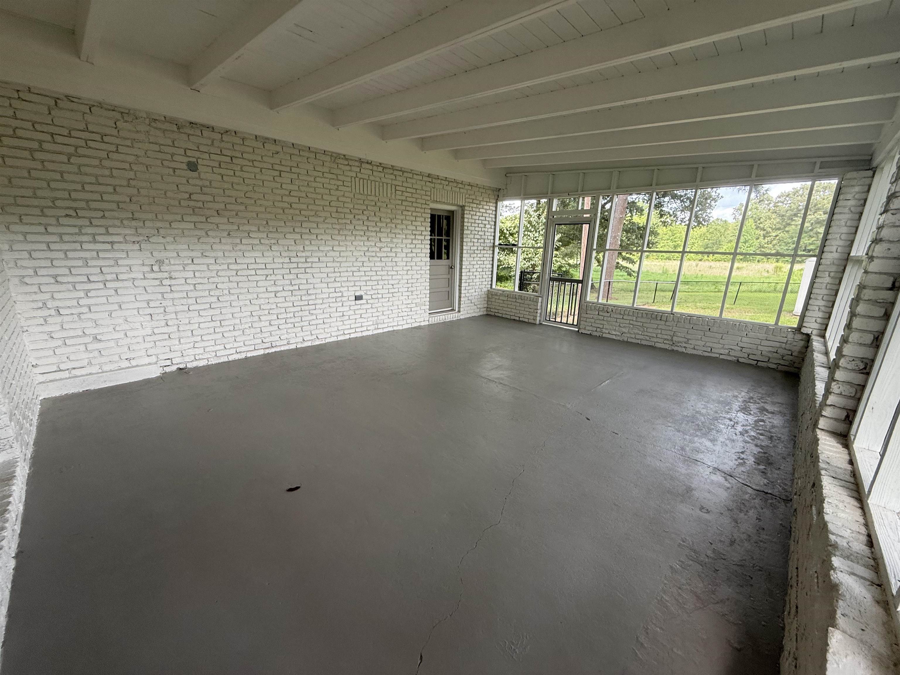 1835 Pleasant Grove Road Moscow, TN 38057 - Photo 27 of 34 Enclosed porch featuring a painted brick wall, concrete flooring, exposed ceiling beams, and a screened exterior wall with a storm door