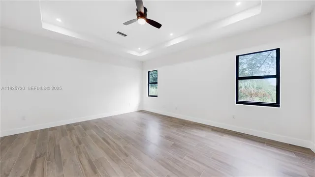 an empty room with wooden floor chandelier fan and windows