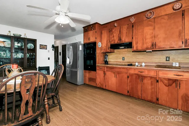 a kitchen with stainless steel appliances granite countertop a refrigerator a sink dishwasher a stove a dining table and chairs with wooden floor