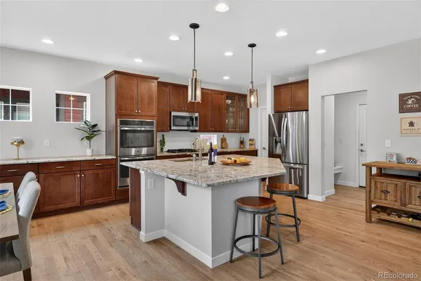 a kitchen with stainless steel appliances granite countertop a refrigerator a stove a sink a dining table and chairs with wooden floor