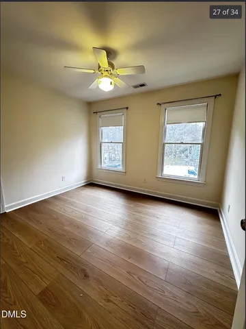 an empty room with wooden floor chandelier fan and windows