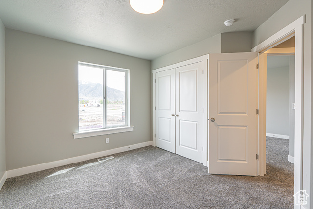 2242 South 1120 West, Unit 69 Logan, UT 84321 - Photo 16 of 26 Unfurnished bedroom featuring carpet flooring, a closet, a mountain view, and a textured ceiling