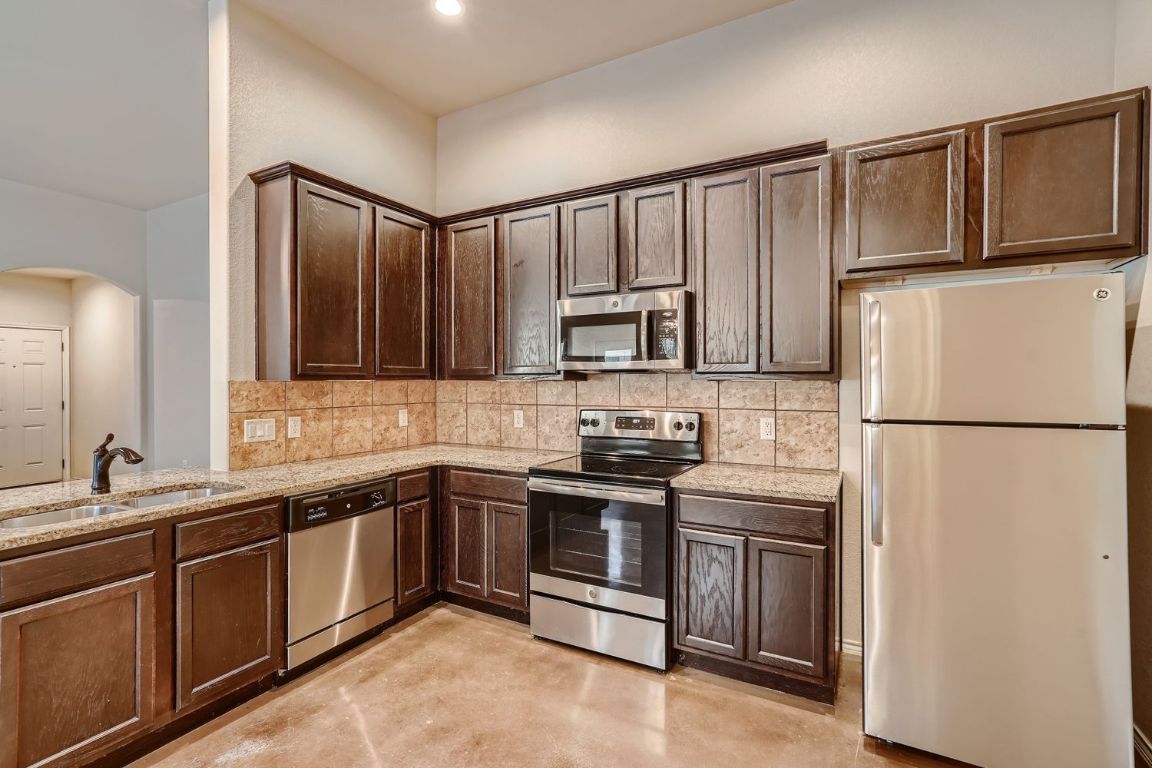 246 Joanne Loop, Unit B Buda, TX 78610 - Photo 4 of 11 Kitchen with tasteful backsplash, appliances with stainless steel finishes, dark brown cabinetry, finished concrete floors, and light stone countertops