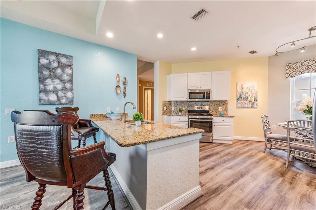 9275 Museo Circle, Unit 103 Naples, FL 34114 - Photo 7 of 49 a kitchen with stainless steel appliances granite countertop a stove top oven a sink a dining table and chairs with wooden floor