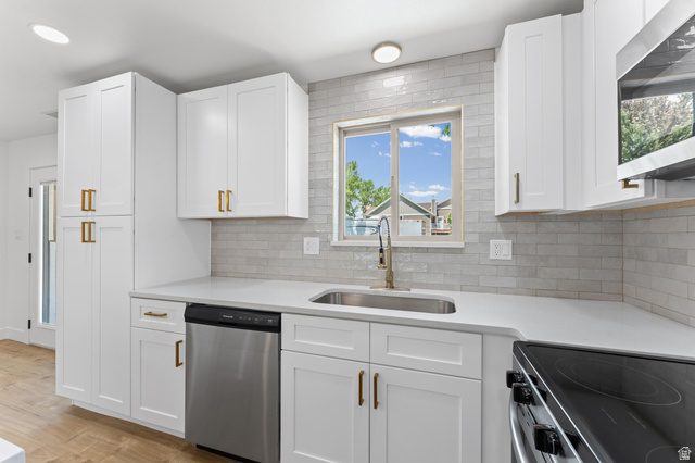 1898 West 600 South Provo, UT 84601 - Photo 7 of 32 Modern kitchen featuring white shaker cabinetry with brass hardware, stainless steel appliances, light countertop surfaces, a subway tile backsplash, and wood-finish flooring