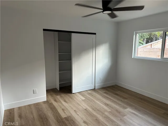 an empty room with wooden floor fan and windows