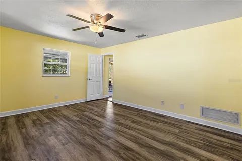 a view of an empty room with wooden floor and a ceiling fan