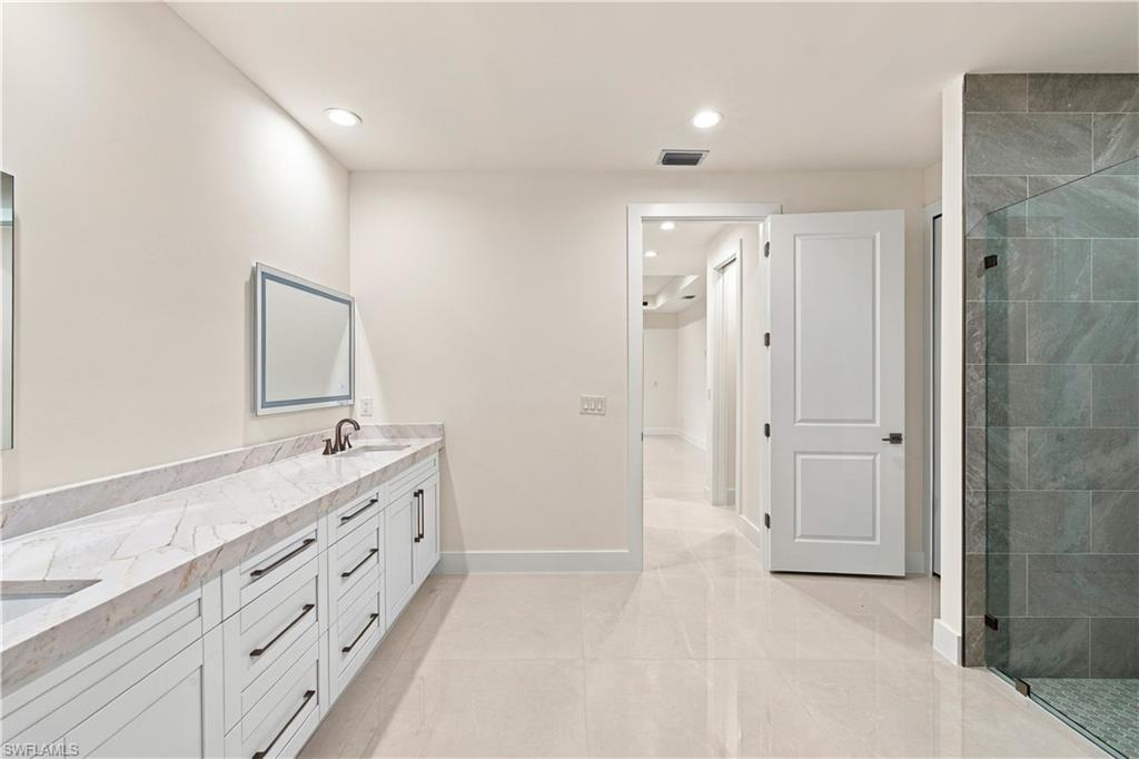 183 5th Street Southwest Naples, FL 34117 - Photo 10 of 40 Dual vanity with a stone countertop, white shaker-style cabinetry, and matte black hardware