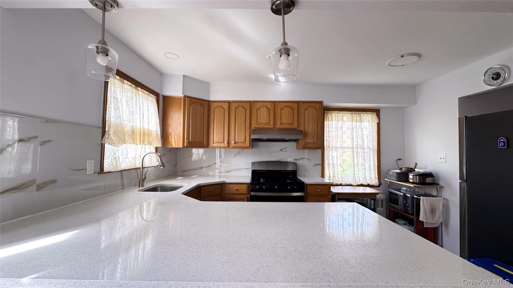 168-12 19th Avenue Queens, NY 11357 - Photo 7 of 27 Kitchen with hanging light fixtures, brown cabinets, stainless steel appliances, light stone counters, and under cabinet range hood
