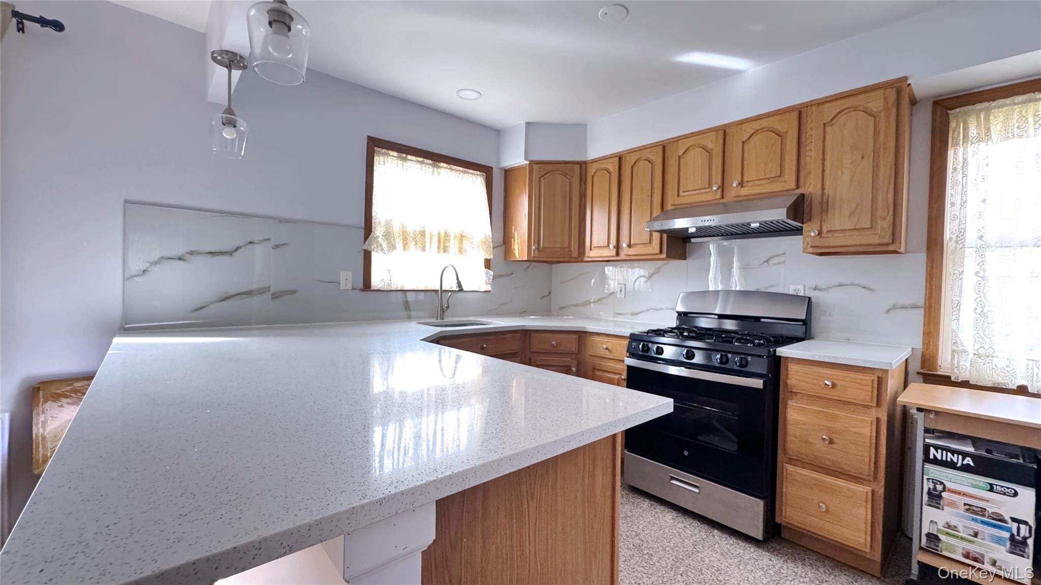 168-12 19th Avenue Queens, NY 11357 - Photo 8 of 27 Kitchen with stainless steel range with gas cooktop, a peninsula, brown cabinetry, under cabinet range hood, and light stone counters