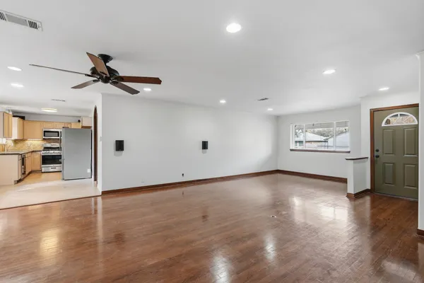 a view of an empty room with wooden floor and a ceiling fan