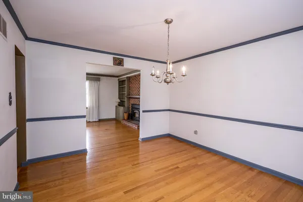 a view of an empty room with chandelier fan and wooden floor