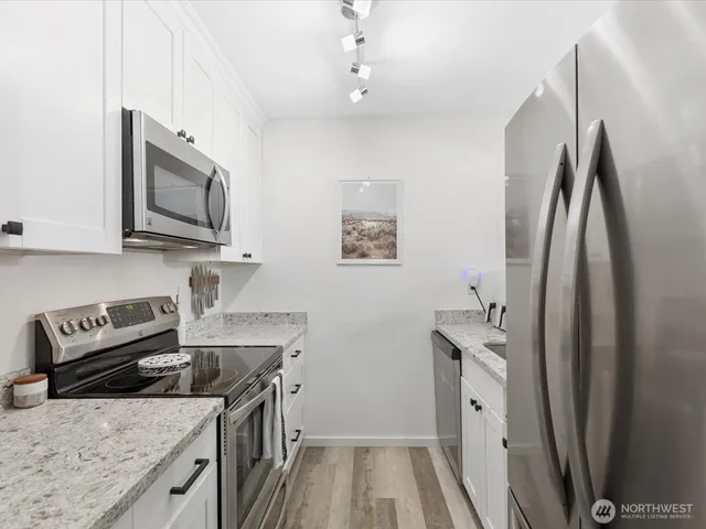 a kitchen with stainless steel appliances granite countertop a refrigerator a stove and a sink with wooden floor