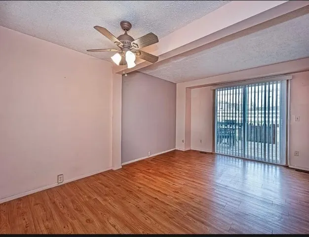 a view of an empty room with wooden floor and a ceiling fan