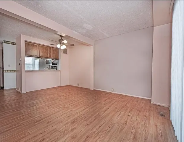 an empty room with wooden floor and kitchen view