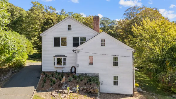 a view of a white house next to a yard with large trees