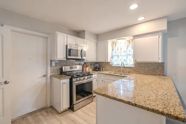 a kitchen with granite countertop a sink a stove top oven and cabinetry