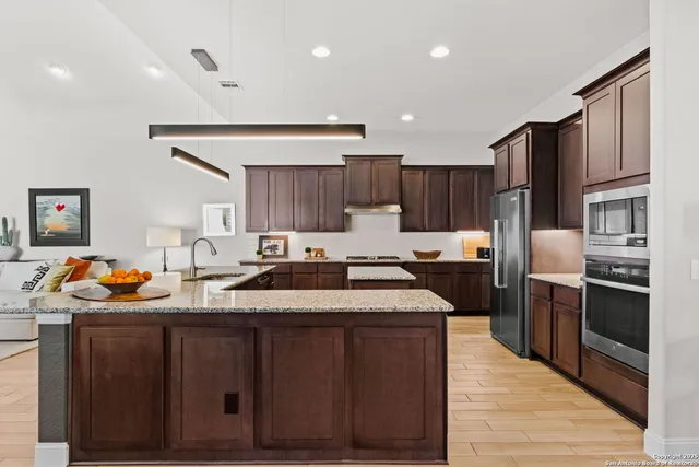 a kitchen with stainless steel appliances granite countertop a refrigerator a sink dishwasher a stove and a oven with wooden floor