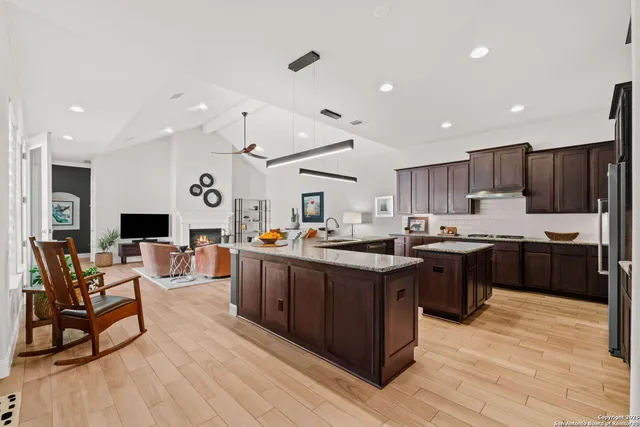 a kitchen with stainless steel appliances granite countertop a refrigerator a sink dishwasher a dining table and chairs with wooden floor