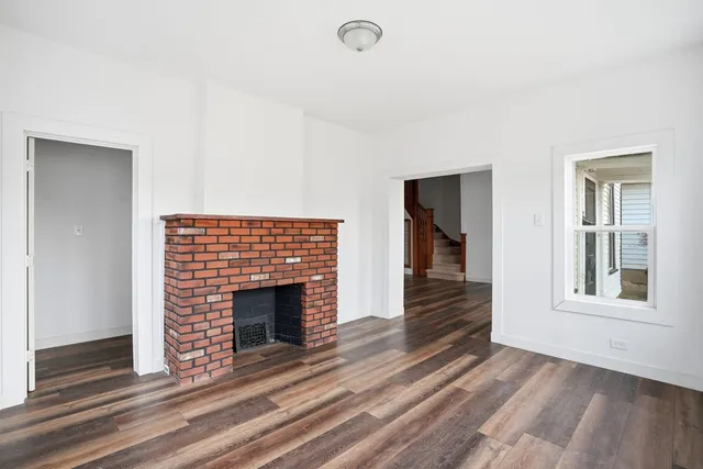 a view of an empty room with wooden floor fireplace and a window