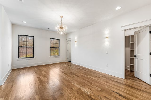 an empty room with wooden floor chandelier and windows
