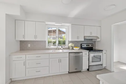 a kitchen with white cabinets appliances a sink and a window