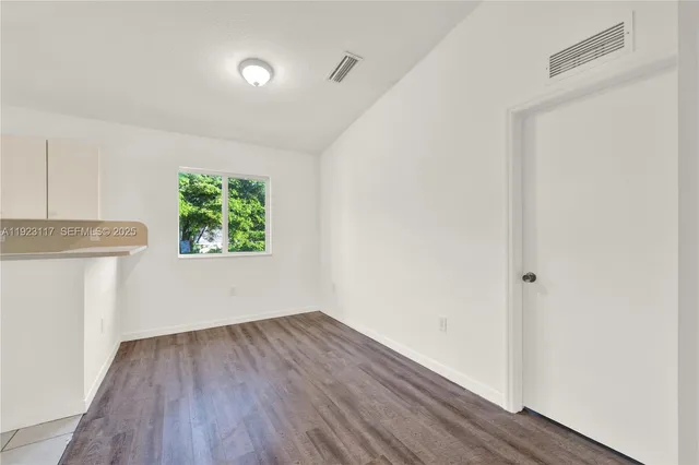 a view of an empty room with wooden floor and a window