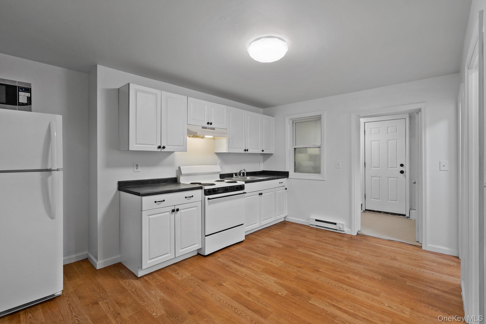 93 Delafield Street Poughkeepsie, NY 12601 - Photo 8 of 27 Kitchen featuring white appliances, white cabinetry, dark countertops, light wood-style flooring, and under cabinet range hood