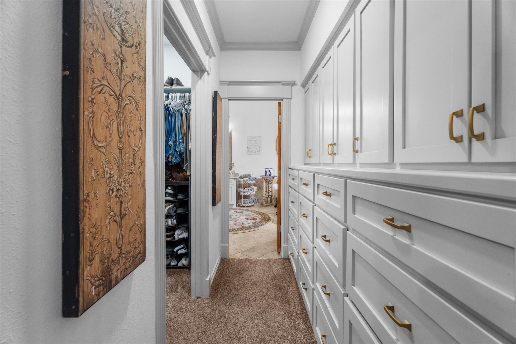 15902 Guinstead Drive Spring, TX 77379 - Photo 19 of 42 Hallway with ample built-in storage cabinets on the right, accented with modern gold handles. To the left, a glimpse of a walk-in closet with organized shelves and clothing racks.