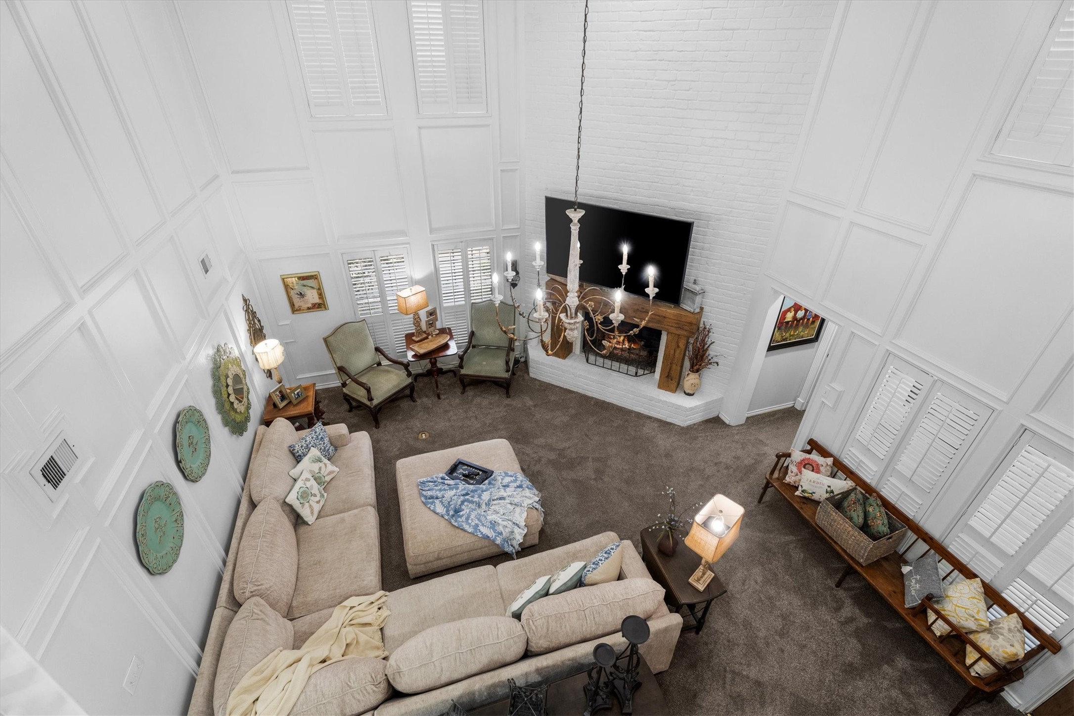 15902 Guinstead Drive Spring, TX 77379 - Photo 26 of 42 Living room featuring a high ceiling with a grand chandelier, large windows with shutters, and a cozy fireplace.
