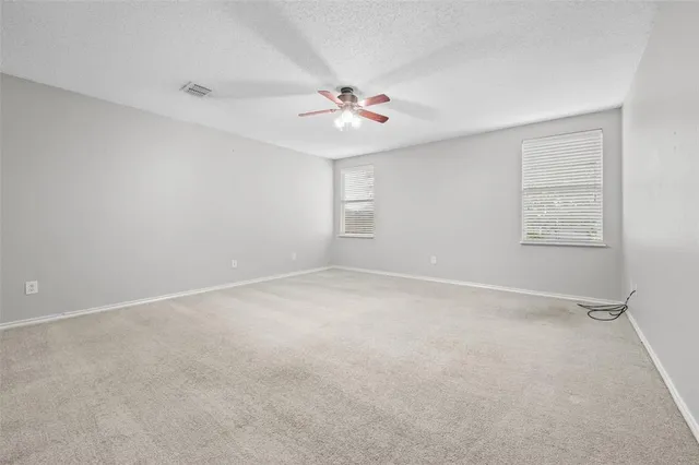 an empty room with chandelier fan and windows