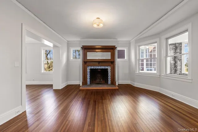 a view of an empty room with wooden floor fireplace and a window