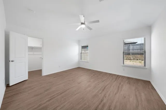 an empty room with wooden floor chandelier fan and windows