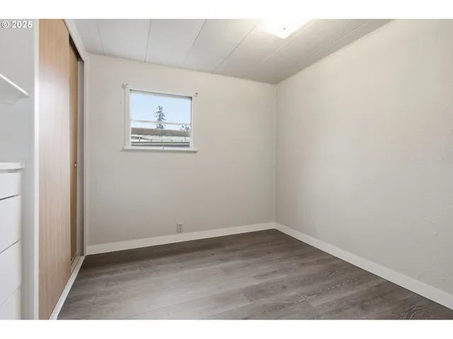 a view of an empty room with window and wooden floor