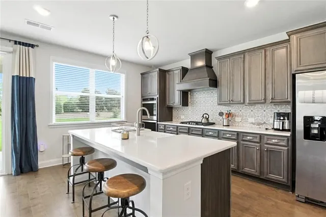 a kitchen with stainless steel appliances a sink a stove a refrigerator cabinets and a dining table with wooden floor