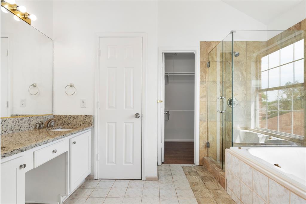 559 Raintree Circle Coppell, TX 75019 - Photo 36 of 40 Bathroom featuring a granite countertop vanity with white cabinetry, a walk-in shower with glass enclosure and natural stone tile, a built-in soaking tub, and a window providing natural illumination