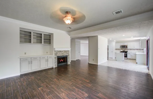 a view of an empty room with wooden floor and a kitchen
