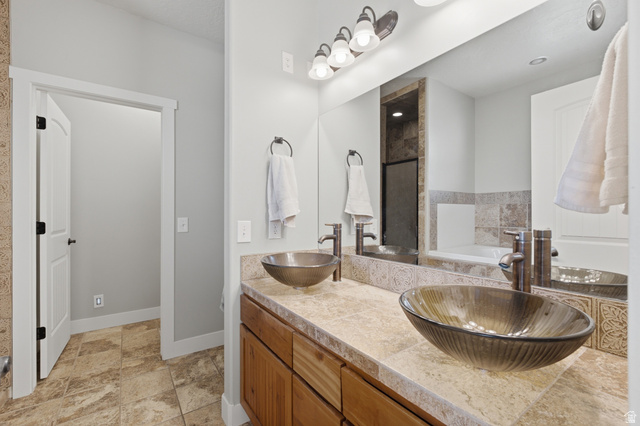 2567 West Rim Rock Drive Stockton, UT 84071 - Photo 25 of 64 Dual vessel sinks set on a stone-look countertop with wood cabinetry, large vanity mirror, and tile flooring
