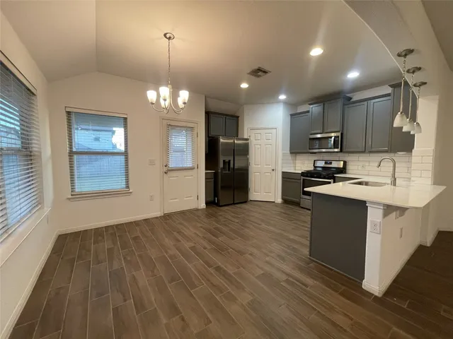 a kitchen with stainless steel appliances granite countertop a refrigerator a sink dishwasher a stove and a dining table with wooden floor