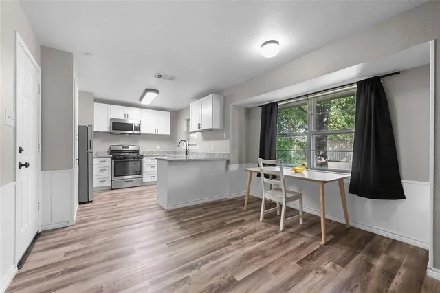 a kitchen with stainless steel appliances granite countertop a stove a refrigerator a sink a dining table and chairs with wooden floor