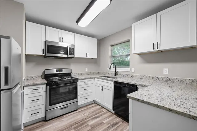 a kitchen with stainless steel appliances granite countertop a stove top oven a sink dishwasher a refrigerator and cabinets with wooden floor