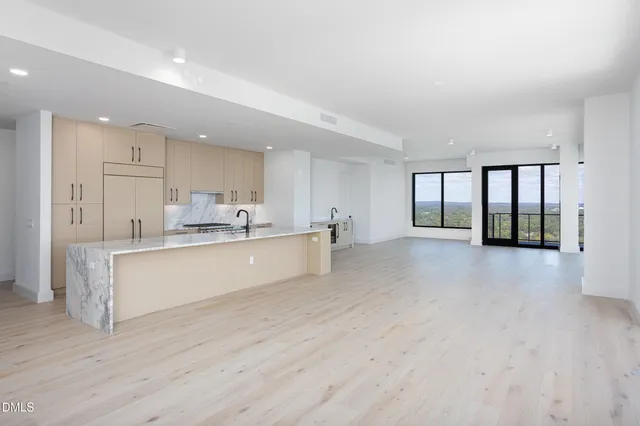 a large white kitchen with kitchen island a sink wooden floor and a large window