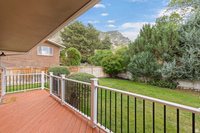 3320 Cherokee Lane Provo, UT 84604 - Photo 42 of 52 Wood-finish deck with white posts and black balusters, featuring a manicured lawn, established greenery, and a mountain backdrop
